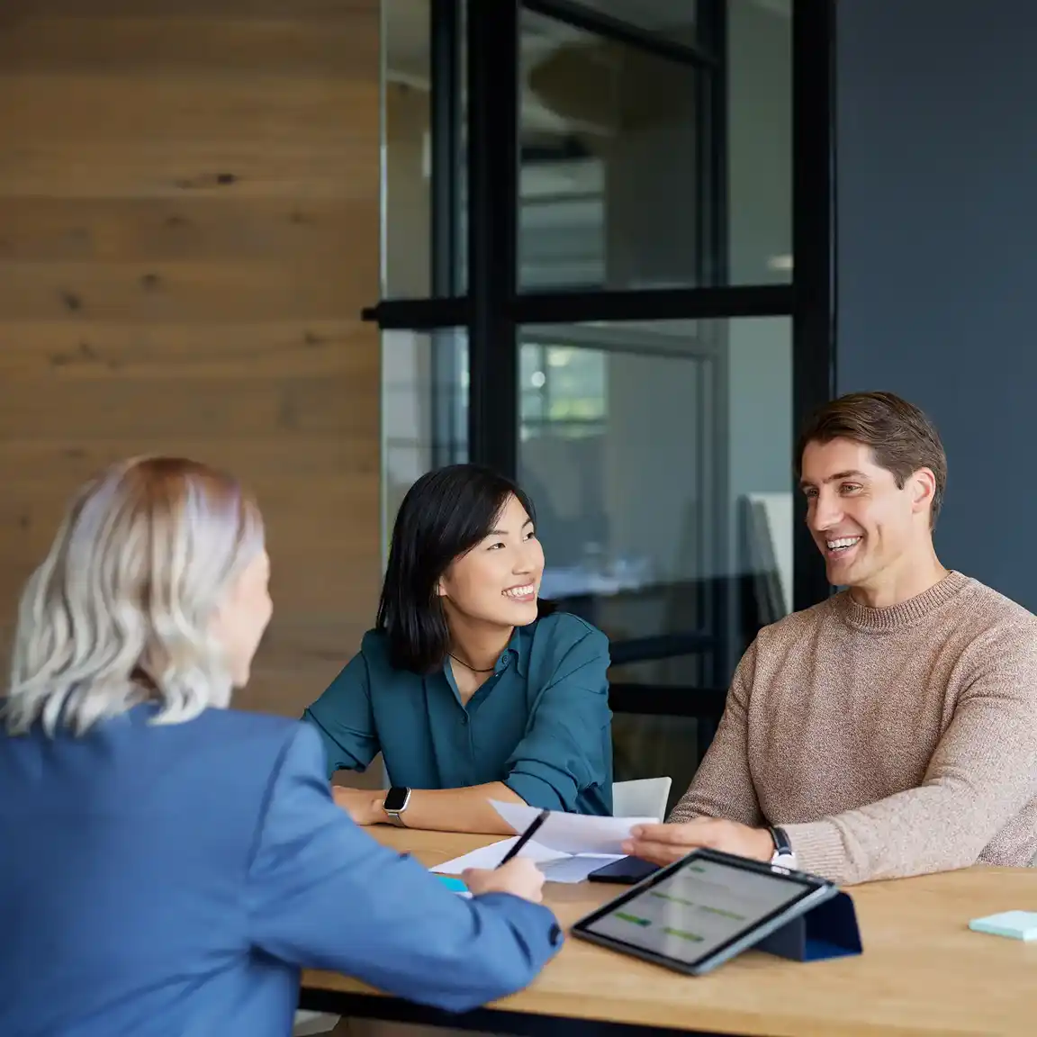 A couple sits at a desk talking with a loan officer about deposit secured loans.