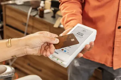 A merchant’s hand holding a Clover Flex credit card reader and a customer’s hand paying by tapping their credit card