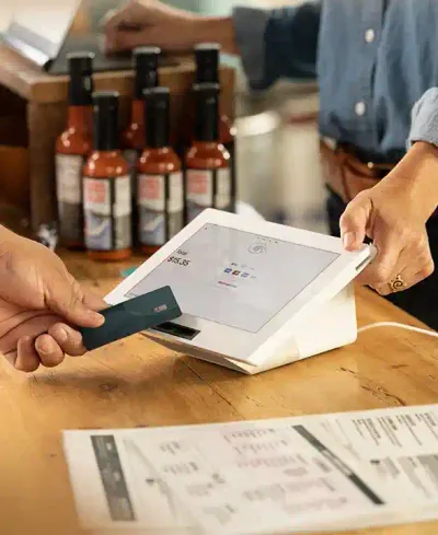  A shopper’s hand holds a credit card up to a Clover Mini point of sale system to process a transaction through tap pay