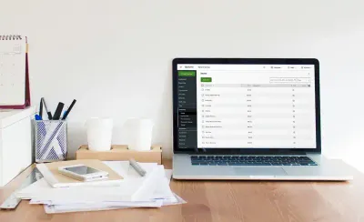 A computer showing the Clover Virtual Terminal for business on its screen sits on a wooden desk with a pile of papers, a notebook, and some pens