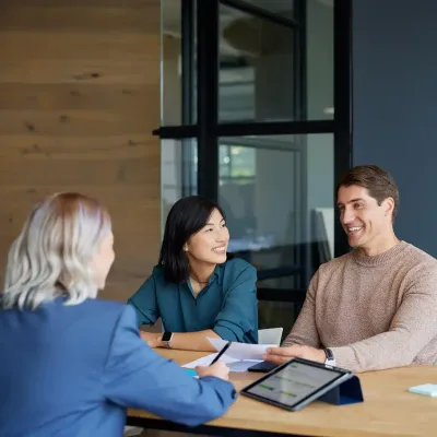 A couple sits at a desk talking with a loan officer about deposit secured loans.