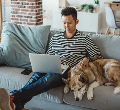 Man and dog looking using laptop on couch