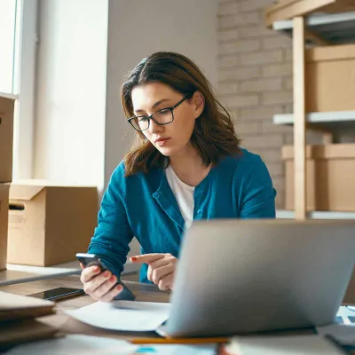 Woman working on computer with phone in hand